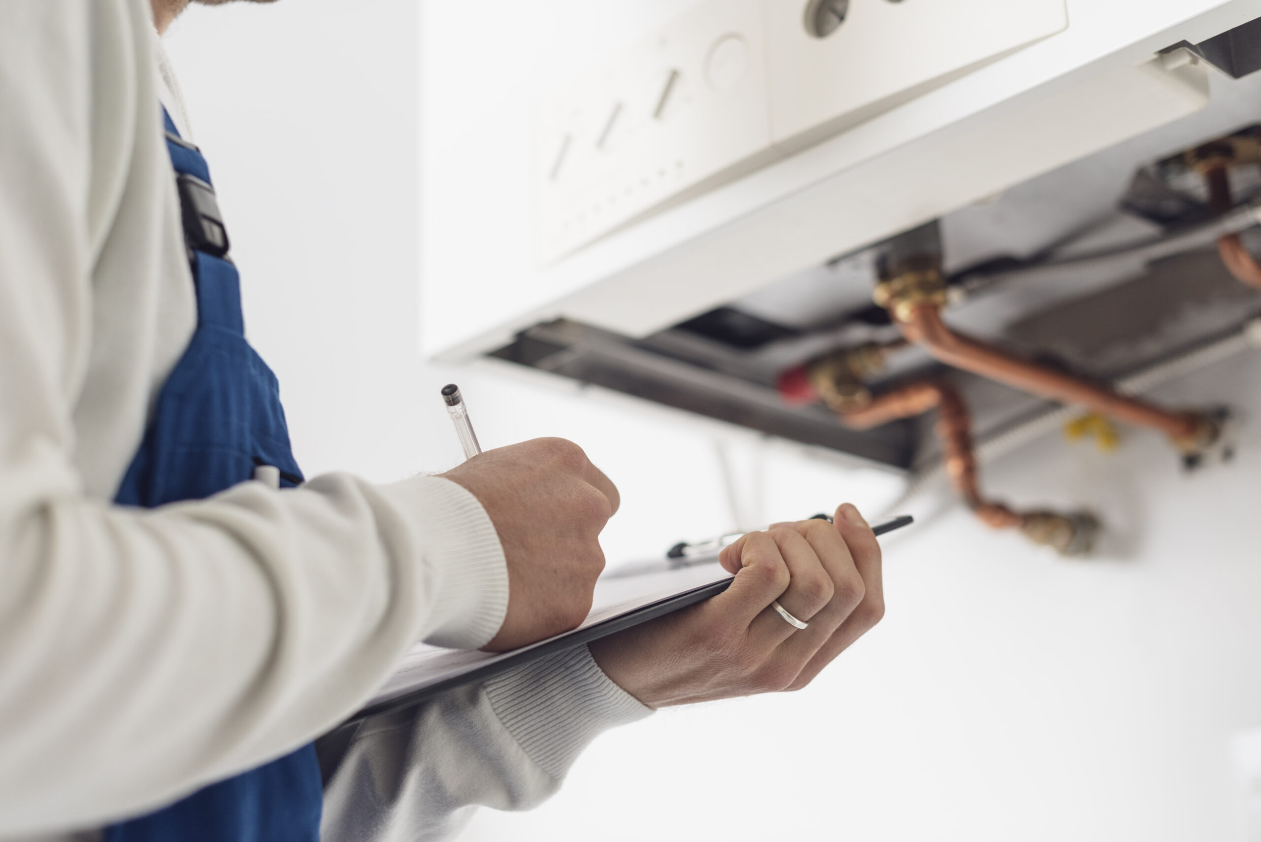 Professional plumber checking a boiler at home and writing on a clipboard